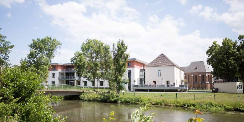 Außenansicht der Seniorenhilfe mit einem Gewässer davor und einem Garten. 