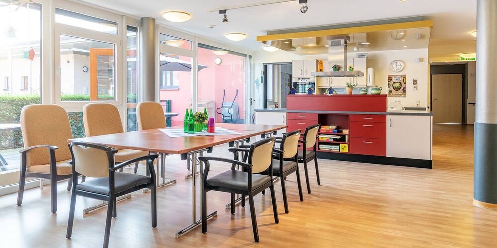 Aufenthaltsraum im Augustinushaus. In diesem steht ein großer Tisch mit vielen Stühlen und einer Küche. 