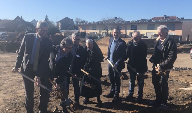 Eine kleine Gruppe von Menschen hat jeweils einen Spaten in der Hand und macht den ersten Stich in die Erde auf einer Baustelle.