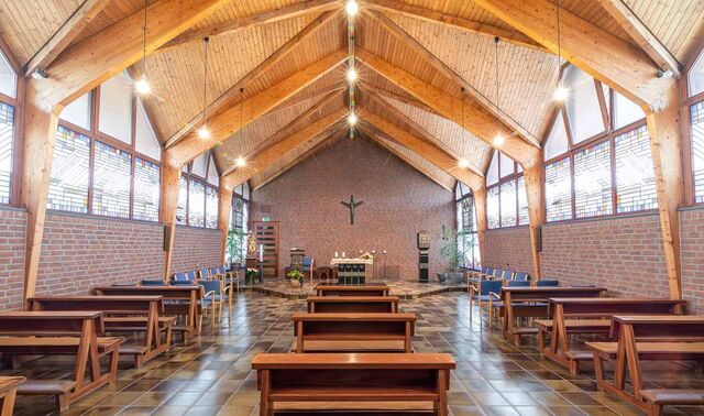 Innenraum der Kapelle des Augustinushaus. In diesem stehen einige Bänke und vorne ist ein Altar. Die Decke der Kapelle ist mit Holz verkleidet. 