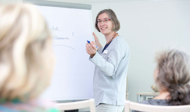 Eine Frau steht vor einem Flipchart und präsentiert einem Publikum etwas. 
