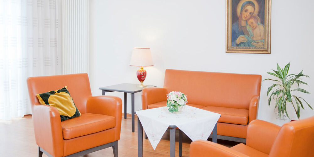 Sitzecke im Haus Maria Hilf mit zwei Sesseln und einem Sofa sowie drei kleinen Tischen. 