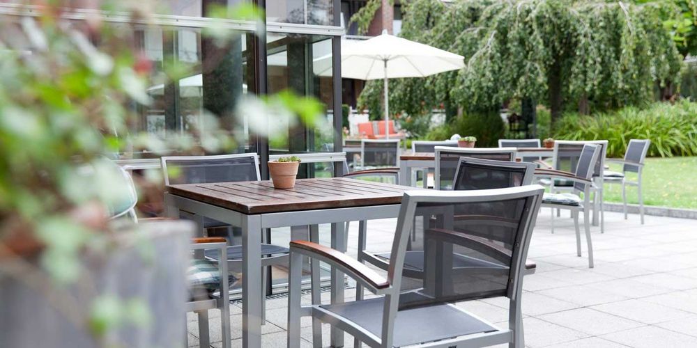 Terrasse und Gartenanlage des Haus Maria Hilf. Auf der Terrasse stehen einige Stühle, Tische und Schirme. 