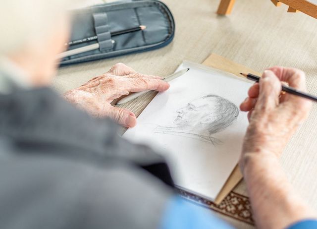 Eine ältere Person zeichnet mit einem Bleistift einen Mann im Profil. 