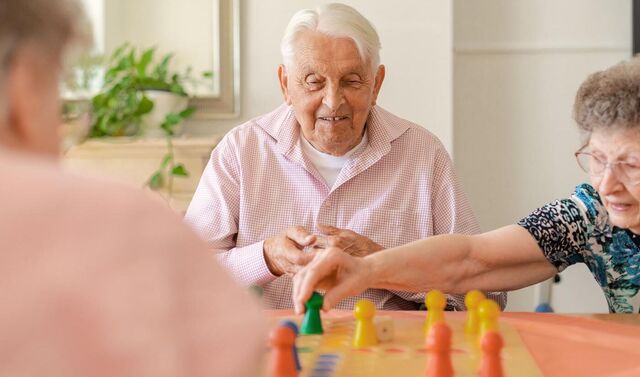 Einige Senioren spielen Mensch ärgere dich nicht.